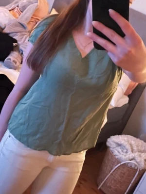 Grön v-ringad blus från Indiska - Säljer en ljusgrön blus från Indiska med v-ringning och korta ärmar. Blusen har en avslappnad passform och är gjord i ett mjukt material som känns skönt mot huden. Perfekt att styla med jeans eller kjol för en enkel och fräsch look. Helt ny och aldrig använd, men lappen är borta. Fin passform, normal i storlek och sitter skönt. Kommer vara väldigt skön i sommar eftersom den är sval och tunn. Storlek M. 