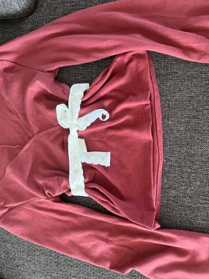 Vinröd långärmad topp med spetsband - Vinröd blus med vida ärmar och djup V-ringning, perfekt för maskerad eller cosplay. Midjan markeras av ett vitt spetsband som knyts framtill. Tillverkad i mjukt tyg med lätt stretch och en figurnära passform. Passar till medeltida eller fantasyinspirerade outfits.