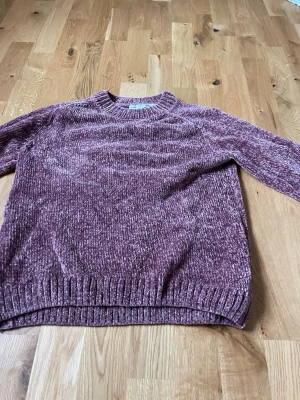 Ljuslila chenilletröja från 157 - Mysig ljuslila stickad tröja från 157 i mjukt chenillematerial. Tröjan har rund halsringning, långa ärmar och ribbade muddar vid ärmslut och nederkant. Perfekt för kalla dagar och ger en avslappnad look.