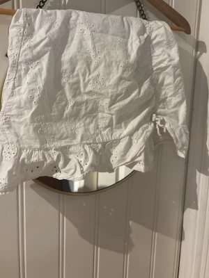 Vit kortkjol med volang och broderi - Söt vit kortkjol med broderade blommor och volangkant. Kjolen har en romantisk känsla med fina detaljer och är perfekt för varma dagar. Tillverkad i lätt bomullstyg som känns luftigt och bekvämt.