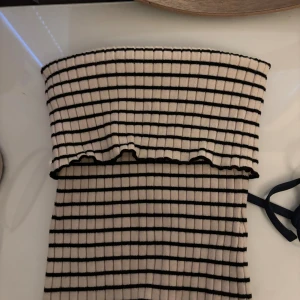 Randig ribbad tubtopp - Säljer en ribbad tubtopp i vitt med svarta ränder. Toppen är axelbandslös och har en stretchig passform som sitter snyggt på kroppen. Köpt från Bershka