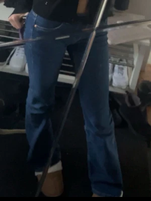 Blå bootcut jeans med låg midja - Säljer ett par klassiska blå bootcut jeans med hög midja och utsvängda ben. Jeansen har fem fickor och stängs med dragkedja och knapp. Perfekta för en avslappnad och trendig look.
