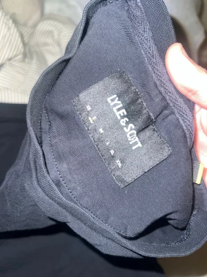 Svart t-shirt från Lyle & Scott - En svart t-shirt från Lyle & Scott med klassisk rund hals och den ikoniska gula logon broderad på bröstet. Tillverkad i mjuk bomull för en bekväm känsla och passar perfekt till jeans eller shorts.