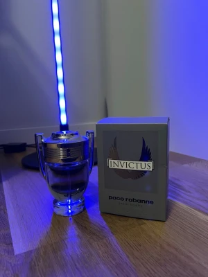 Invictus parfym - Fräsch och maskulin parfym från Paco Rabanne, Invictus. Flaskan har en unik design som liknar en pokal i genomskinligt glas med silverfärgade detaljer. Förpackningen är grå med blå och silverdetaljer och har Invictus-loggan med vingar på framsidan. Ny pris ca 500-700kr