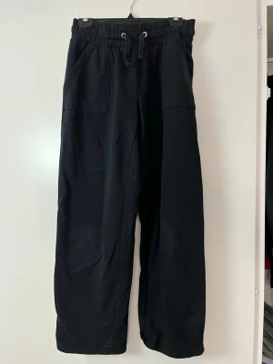 Svarta mjukisbyxor med dragsko - Säljer ett par svarta mjukisbyxor med breda ben och dragsko i midjan. Byxorna har två fickor fram och två bakfickor. Perfekta för chill dagar och riktigt sköna tack vare det mjuka materialet. Passar dig som gillar en avslappnad stil.