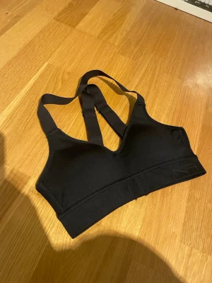 Svart sport-bh från new apparel - Säljer en svart sport-bh från new apparel med brottarrygg och bred resår under bysten. Tillverkad i ett stretchigt material som passar perfekt för träning. Enkel och stilren design med diskret logga på sidan. Aldrig provad, skickar gärna med PostNord😄