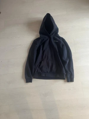 Mörkblå hoodie från Peak Performance - Snygg mörkblå hoodie från Peak Performance med klassisk huva och magficka. Diskret logga på bröstet och ribbade muddar vid ärmslut och nederkant. Perfekt för en avslappnad och stilren look.