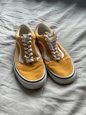 Gula Vans Old Skool sneakers - Gula Vans Old Skool sneakers med vit sula och klassisk vit sidorand. Ovandel i mocka och canvas, vita skosnören och gummisula med rutmönster. Perfekta för en avslappnad streetstil.