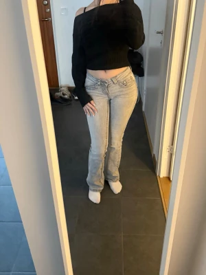 Ljusgrå bootcut jeans med låg midja - Säljer ett par ljusgrå bootcut jeans med låg midja och klassiska fem fickor. Jeansen har en snygg, avslappnad passform och är perfekta för en trendig vardagslook. Materialet är denim och de har en stilren design utan slitningar eller dekorationer.