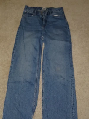 Blå begi jeans med rå kant - Ett par klassiska blå jeans som är begi jens passform och rå, fransig kant nertill. Jeansen har fem fickor och stängs med dragkedja och knapp. Perfekta för en avslappnad och trendig look.