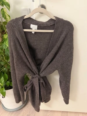 Mörkbrun kofta från H&M med knytband - Mysig mörkbrun kofta från H&M med långa ärmar och knytband framtill. Koftan är stickad i mjukt material och har en avslappnad passform, perfekt att slänga över en topp eller t-shirt. Enkel och stilren design som passar till det mesta.