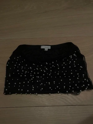 Svart kjol - Svart kjol från Hot & Delicious i storlek S. Toppen är dekorerad med pärlor över hela ytan och har en transparent känsla. Perfekt för att ge din outfit en unik och trendig touch.