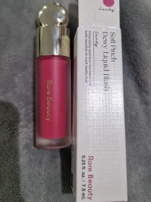 Rare Beauty Soft Pinch Dewy Liquid Blush - Rare Beauty Soft Pinch Dewy Liquid Blush i färgen Lucky. Flytande rouge med intensivt rosa nyans och dewy finish. Kommer i en frostad glasflaska med silvrig rundad kork. Perfekt för att ge kinderna en fräsch och naturlig lyster.