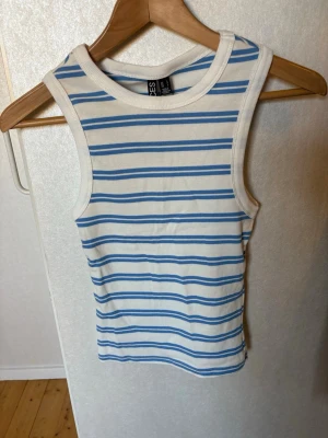 Randig linnetopp från Pieces - Snygg ärmlös linnetopp från Pieces i vitt med blåa ränder. Toppen har rund halsringning och är tillverkad i mjuk bomull, perfekt för varma dagar. Enkel och fräsch design som passar till mycket.
