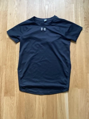 Svart träningströja från Under Armour - Svart kortärmad träningströja från Under Armour med rund hals och logga på bröstet. Tillverkad i ett lätt och snabbtorkande material som passar perfekt för träning och sportaktiviteter.