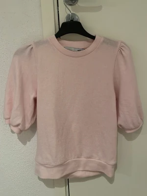 Ljusrosa topp med puffärm - Supersöt ljusrosa stickad topp med puffiga kortärmar och rund hals. Tillverkad i mjukt material som känns skönt mot huden. Perfekt för dig som vill ha en enkel men ändå trendig look. 