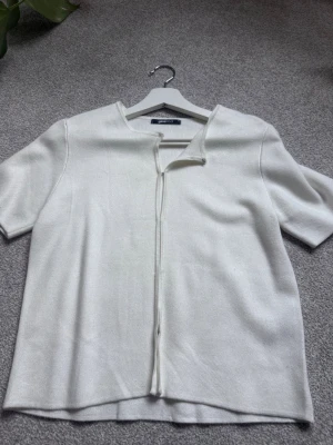 Vit kortärmad kofta från gina tricot - Stilren vit kofta från gina med korta ärmar och öppen front som stängs med diskreta krokar. Tillverkad i ett mjukt, tunt stickat material som ger en clean och modern look. Perfekt att slänga över en topp för en enkel men snygg outfit.
