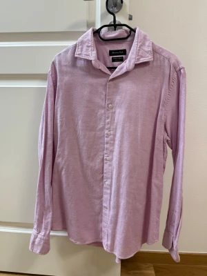 Ljusrosa manchesterskjorta Massimo Dutti - Ljusrosa skjorta från Massimo Dutti i mjuk manchester. Klassisk krage, knäppning framtill och långa ärmar. Perfekt för dig som gillar en avslappnad men ändå stilren look.