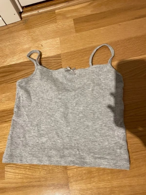 Grå ribbad linnetopp med rosett - Snygg grå ribbad linnetopp med smala axelband och en liten rosett framtill. Perfekt för lager-på-lager eller till jeans. Mjuk och stretchig känsla, passar dig som gillar enkel och stilren look. Skickar helst med PostNord😊