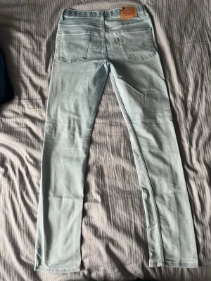 Ljusblå Levi's slim jeans - Stroken 16a men sitter som 30x32. Säljer ett par ljusblå slim jeans från Levi's med klassiska fem fickor och läderpatch bak i midjan. Jeansen har en smal passform och är tillverkade i stretchigt denimtyg för extra komfort. Perfekta för en avslappnad och trendig look.