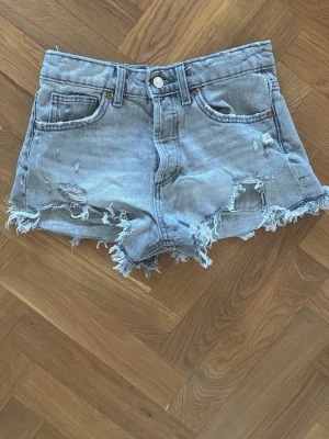 Ljusgråa jeansshorts - Säljer ett par ljusgråa jeansshorts med slitna detaljer och fransig kant. Shortsen har cool stil. Perfekta för sommardagar och ger en avslappnad vibe.