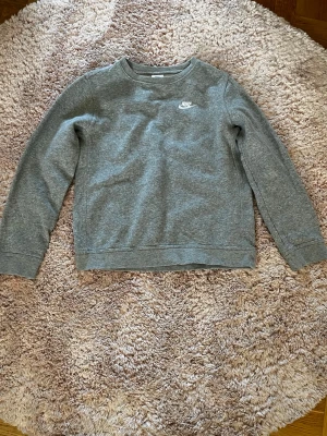 Grå sweatshirt från Nike - Klassisk grå sweatshirt från Nike med rund halsringning och diskret Nike-logga broderad på bröstet. 
