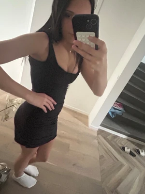 Svart tight kortklänning - En svart, tight kortklänning med ärmlös design och rundad urringning. Klänningen har en enkel och stilren look som framhäver figuren. Perfekt för dig som gillar minimalistisk stil och vill ha något klassiskt i garderoben.