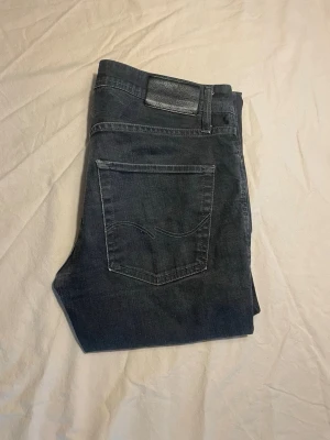 Mörkgrå jeans från Nudie Jeans - Goa vintage Jack n Jones Jeans med klassisk femficksmodell och raka ben. Jeansen har en väldigt simpel tvätt och är rätt styva denim lappen är dessutom bort klippt men skulle storleken är ungefär 32/34. Köp dom ba🥰