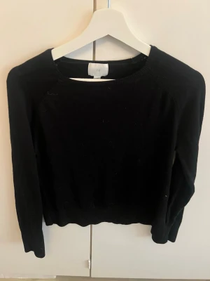 Svart stickad tröja från H&M - En enkel och stilren svart stickad tröja från H&M. Tröjan har rund halsringning, långa ärmar och ribbade muddar vid ärmslut och nederkant. Perfekt basplagg att matcha med allt i garderoben.