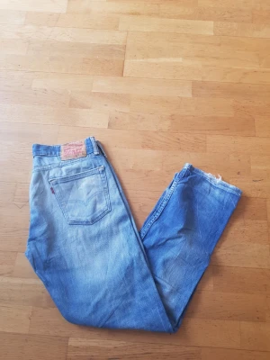 Levi's 513 ljusblå jeans - Ljusblå Levi's 513 jeans med klassisk femficksdesign och rakt ben. Jeansen har en vintagekänsla med slitningar och råa benslut. Tillverkade i bomull med Levi's ikoniska läderpatch bak i midjan.