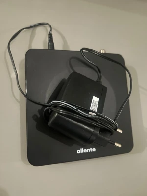 Allente digital TV-box med adapter - Digital TV-box från Allente i svart, med tillhörande strömadapter. Boxen har HDMI, USB, RJ-45 och antennuttag samt stöd för Dolby Audio och WiFi. Kompakt och fyrkantig design, perfekt för streaming och TV-kanaler.