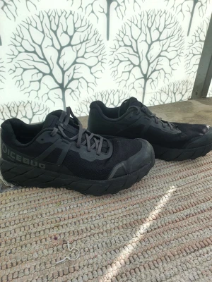 Svarta Icebug sneakers - Säljer ett par svarta sneakers från Icebug med robust sula och meshmaterial på ovansidan. Skorna har klassisk låg profil och tydliga logodetaljer på sidan. Perfekta för dig som vill ha både stil och funktion.