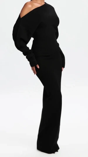 Svart offshoulder långklänning - Snygg svart långklänning med offshoulder-design och långa ärmar. Klänningen har en figurnära passform och är tillverkad i ett stickat material som ger en mjuk och bekväm känsla. Perfekt för dig som vill ha en stilren och trendig look.