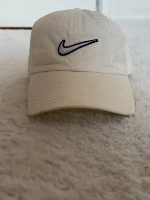 Vit keps från Nike med broderad logo - Snygg vit keps från Nike med klassisk broderad svartvit swoosh-logga framtill. Kepsen har böjd skärm och justerbar passform baktill. Tillverkad i bomullstyg som ger en clean och sportig look.