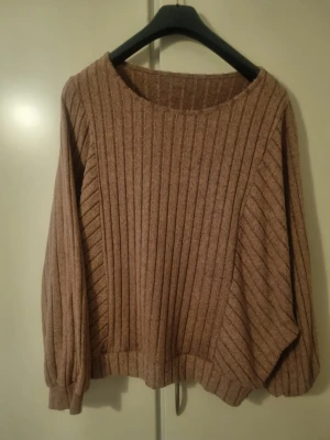 Mörkrosa/brun - Mysig brun stickad tröja med breda ribbor och rund hals. Tröjan har en avslappnad passform och långa ärmar med lätt puff vid mudden. Perfekt för lager på lager och enkel att matcha till olika outfits.