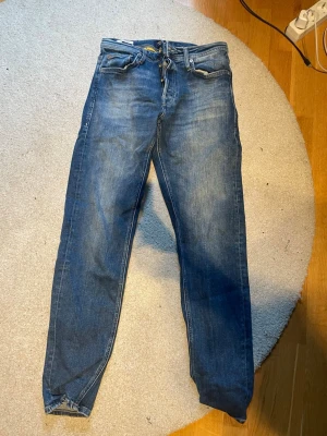Blå tapered jeans från Jack & Jones - Säljer ett par blå jeans från Jack & Jones, modell Tapered/Mike. Jeansen har klassisk femficksdesign, gul söm och avsmalnande ben. Perfekta för dig som gillar en avslappnad men ändå snygg stil.