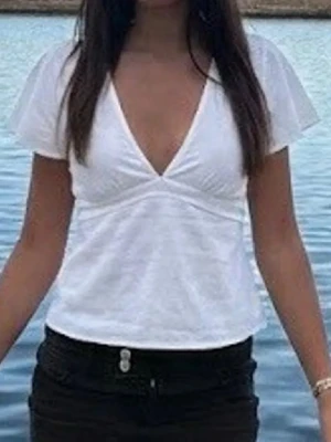 Vit omlott blus med knytband - Snygg vit blus med omlott-design och v-ringning. Toppen har korta, luftiga ärmar och knytband i ryggen som ger en fin passform. Perfekt för dig som gillar en enkel men stilren look. Materialet känns mjukt och lätt.