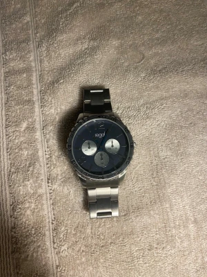 Silverfärgad klocka från Regal - Stilren klocka från Regal med silverfärgat armband och blå urtavla. Klockan har tre mindre urtavlor och ett robust metallarmband som ger en modern look. Perfekt för dig som gillar klassiska accessoarer med en twist.