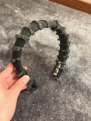 Svart diadem med fransar från lexi uf - Unikt svart diadem från lexi uf, tillverkat i tyg med råa, fransiga kanter för en edgy och trendig look. Diademet är vadderat och har en bred form som ger extra volym. Perfekt accessoar för dig som vill sticka ut och addera en cool detalj till din outfit.