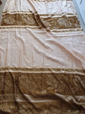 Beige och brun filt med rosor - Säljer en stor vanlig gardin i beige och brunt med vackert blommönster. Gardinens kanter har en fin fransdetalj som ger en extra touch av stil. Längd: 248 cm och Bredd: 141cm. (Det är en gardin men vet inte vilken slags men den är inte så tunn)