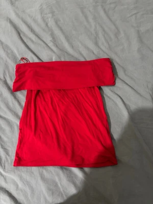 Röd offshoulder tröja  - Trendig röd tröja  i mjukt tyg med offshoulder-design. Tröjan  har en åtsittande passform och lätt rynkade detaljer längs sidorna för en snygg siluett. Perfekt för dig som vill sticka ut med en färgstark look. Den har dock en liten hål i sig