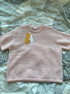 Ljusrosa stickad topp Gina Tricot - Supersöt ljusrosa stickad topp från Gina Tricot med korta ärmar och rund halsringning. Perfekt för dig som gillar en enkel men mysig stil. Materialet känns mjukt och toppen har en rak passform som är lätt att matcha med olika outfits. Plagget är helt nytt och har kvar prislapp.