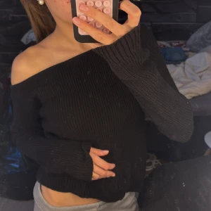 Svart off shoulder stickad tröja - Trendig svart stickad tröja med off shoulder-design och långa ärmar. Tröjan har en ribbad struktur och en avslappnad passform som ger en snygg och bekväm look. Perfekt att styla med jeans eller kjol för en cool vardagsoutfit. Det står inte storlek i men skulle säga at den skulle passa xs-M 