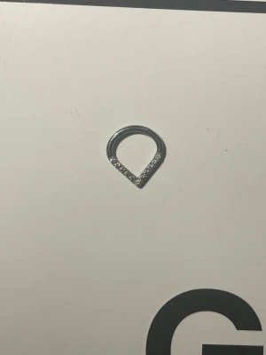 Silverfärgad ring med stenar - Septum Unik ring i silverfärg med droppformad design. Ena sidan av ringen är dekorerad med små gnistrande stenar som ger en elegant touch. Perfekt för dig som gillar stilrena och moderna accessoarer.