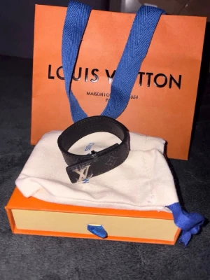 Louis Vuitton svart läderarmband - Snyggt svart armband från Louis Vuitton i läder med klassiskt LV-spänne i silverfärg. Armbandet har en stilren design med diskret mönster på lädret och justerbar längd. Perfekt accessoar för att lyfta din outfit.
