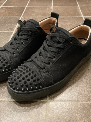  Louboutin skor - Säljer ett par svarta sneakers från Christian Louboutin med nitar. Bortsett från skadorna på insidan och fläcken man ser på bild 5 är de i bra skick, fläcken är dock inte så synlig när man har på sig dem. Tvättar innan jag skickar. Tveka inte på att höra av dig vid frågor😁