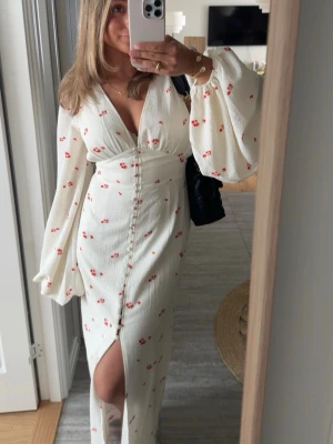 Adoore klänning - Supersöt vit maxiklänning med små röda blommor, djup v-ringning och långa puffärmar. Endast använd ett fåtal gånger!! Nypris : 1695kr