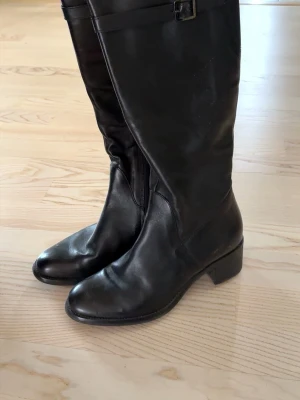 Tamaris - Svarta knähöga stövlar - Svarta knähöga stövlar med blockklack och dragkedja på sidan. Bekväma och stabila att gå i. Klackhöjden är 4,5 cm.