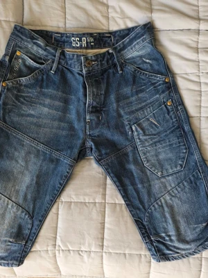 Blå jeansshorts från G-star  - Snygga blå jeansshorts från GS-R med flera fickor och coola sömdetaljer. Shortsen har knäppning med knappar och klassisk femficksdesign. Perfekta för en avslappnad stil under varmare dagar.