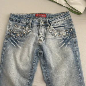 Ljusblå 2000s tal jeans  - Snygga ljusblå jeans från River Jeans med slitningar, silverfärgade nitar vid fickorna och broderade bakfickor.